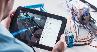 Person hält ein Tablet vor elektronischen Bauteilen. Foto: PROFACTOR