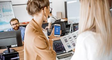 Zwei Frauen mit einem Smartphone in einem Büro. Foto: depositphotos/rossandhelen