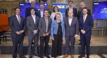 Neun Männer und zwei Frauen in eleganter Bekleidung posieren für ein Gruppenbild im Technischen Museum in Wien vor Roll-Ups